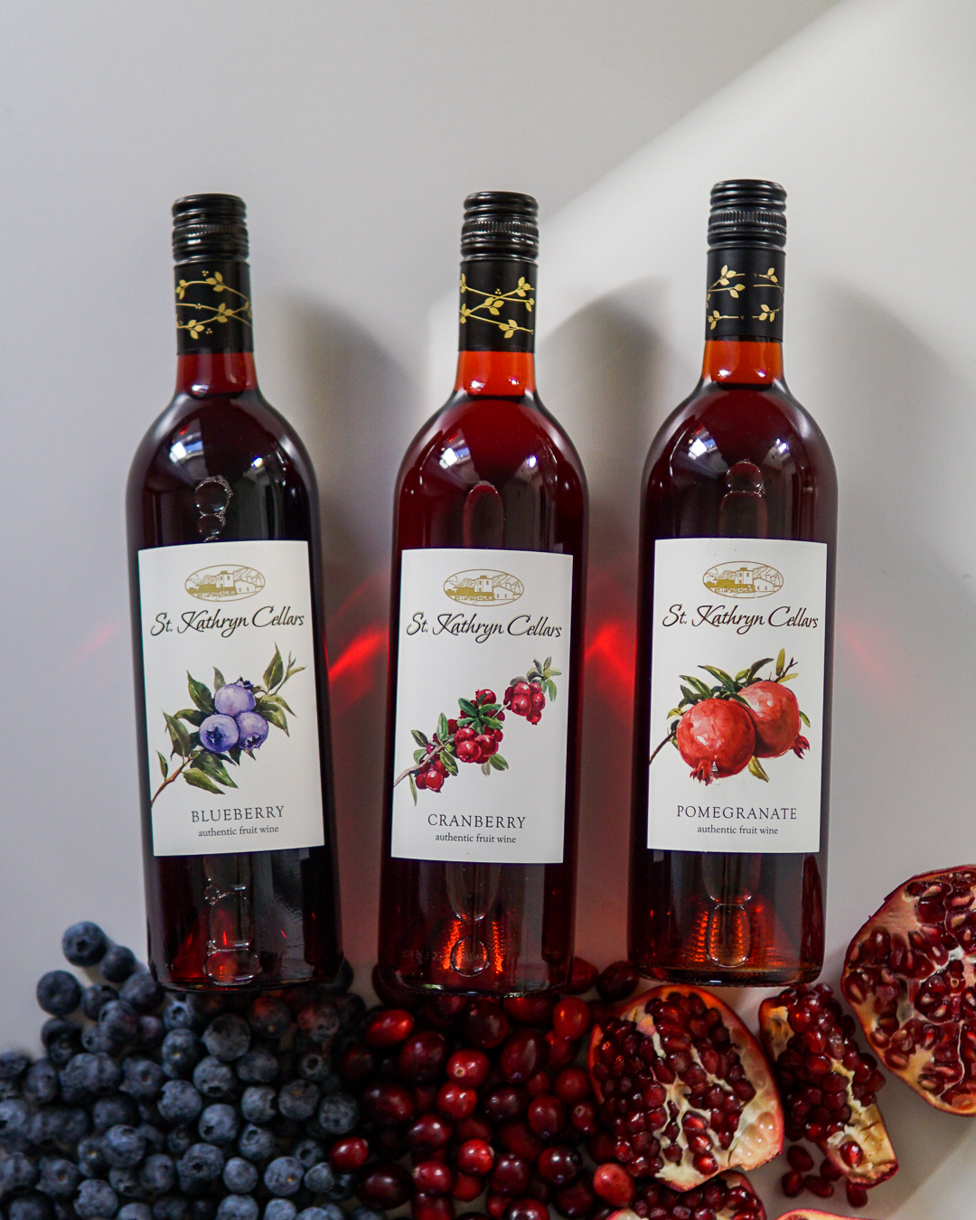 Bottles of blueberry, cranberry, and pomegranate wines with coordinating fruit below each bottle.